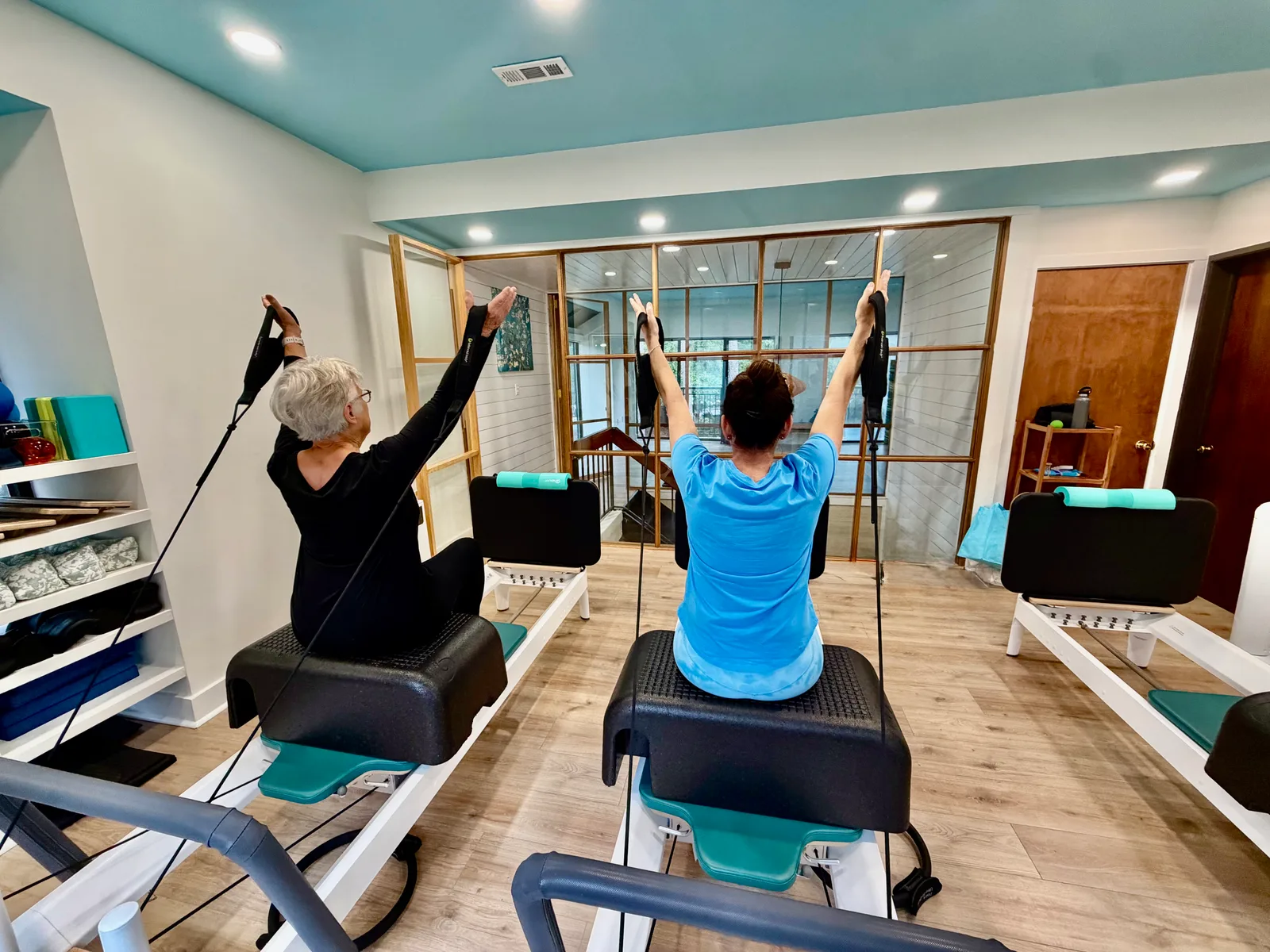 Two clients reaching overhead on reformers in the bright, airy Blue Sky Pilates studio on Hilton Head Island
